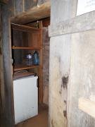 Blick schräg in den Kellerschuppen. Es befinden sich dort ein Regal für Lebensmittel, ein Kühlschrank und zwei Steckdosen. 